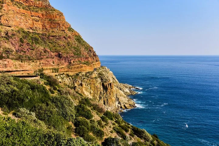 A road winds along the edge of a rocky cliff beside the deep blue sea.
