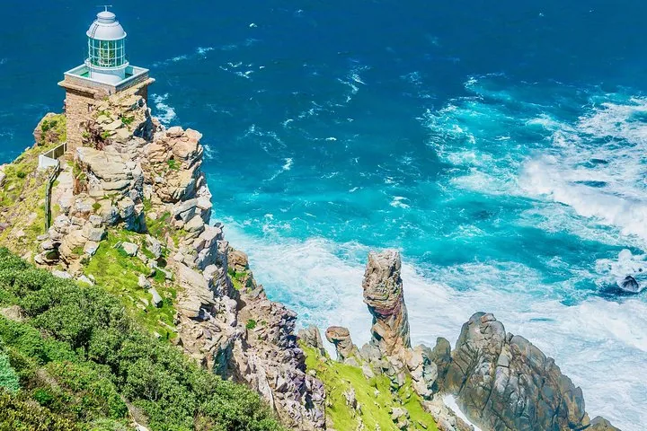 Ein Leuchtturm steht auf einer felsigen Klippe und blickt auf leuchtend türkisfarbene, tosende Wellen.