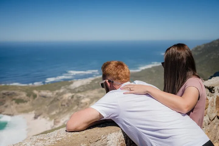 Ein Paar lehnt an einer Steinmauer und genießt den weiten Blick aufs Meer.
